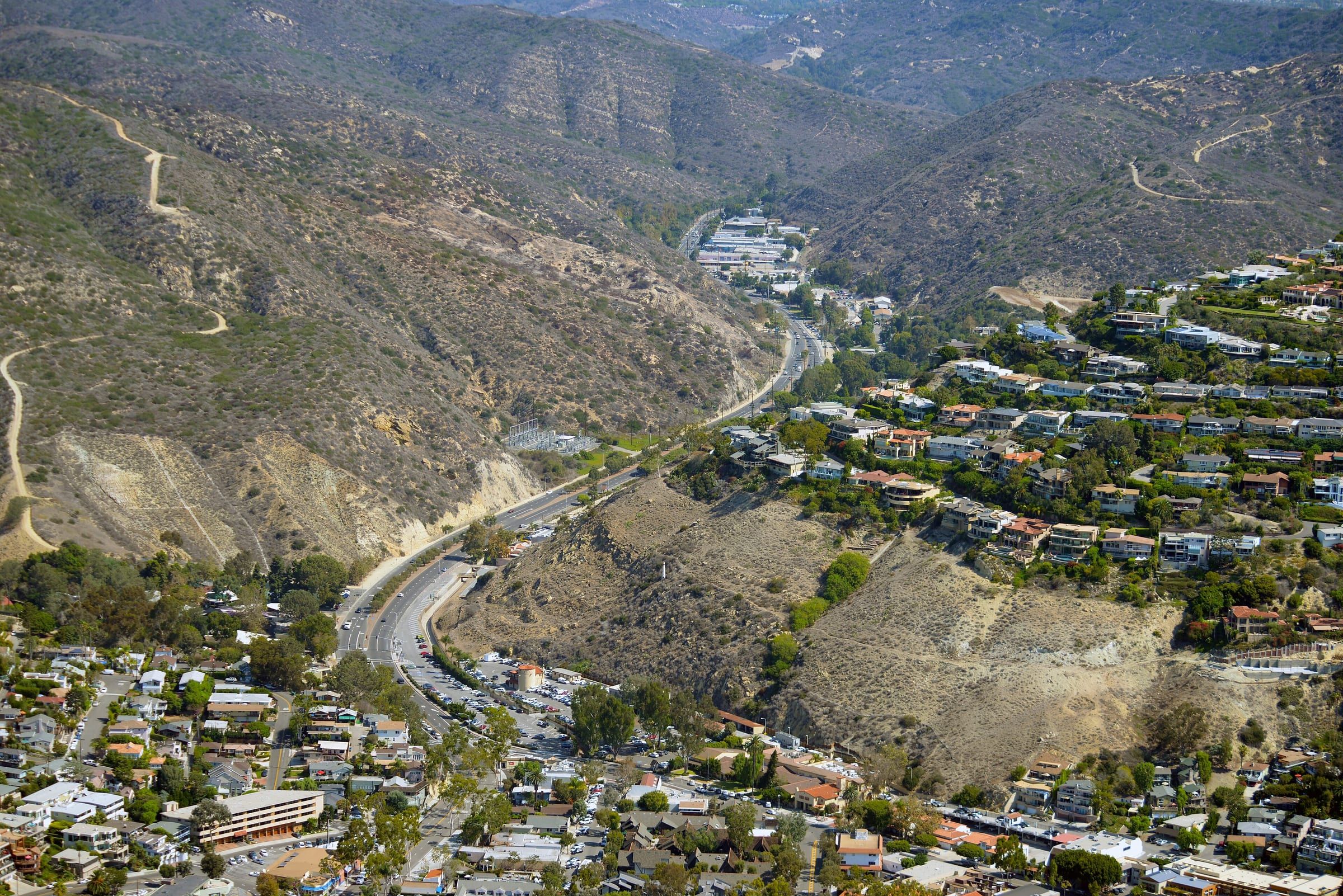 Aerial view of Laguna Canyon Road winding down the canyon to downtown Laguna Beach, with hillside homes on one side