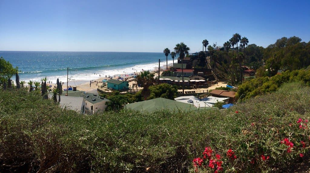 Crystal Cove's Historic District seen from the bluff, with beach cottages among palms and a sandy beach and surf beyond